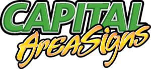 Capital Area Signs logo featuring two-line text design. Top lineCAPITAL' in bold, block sans-serif font with bright green color, white highlights, white inner outline, black outer outline, and dark gray drop shadow. Bottom line 'AreaSigns' in flowing script font with gradient from yellow to orange, subtle highlights, light orange inner outline, black outer outline, and dark gray drop shadow. Both text elements have three-dimensional glossy appearance with overlapping composition creating a dynamic, energetic business logo for a signage company.